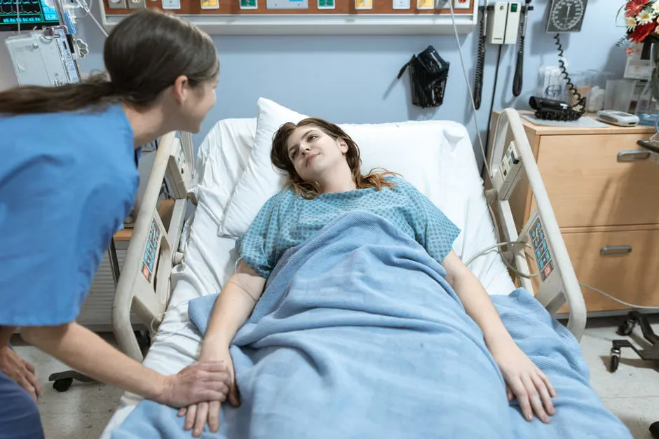 Nurse at a hospital bedside responding to a patient call from a wall-mounted nurse call station
