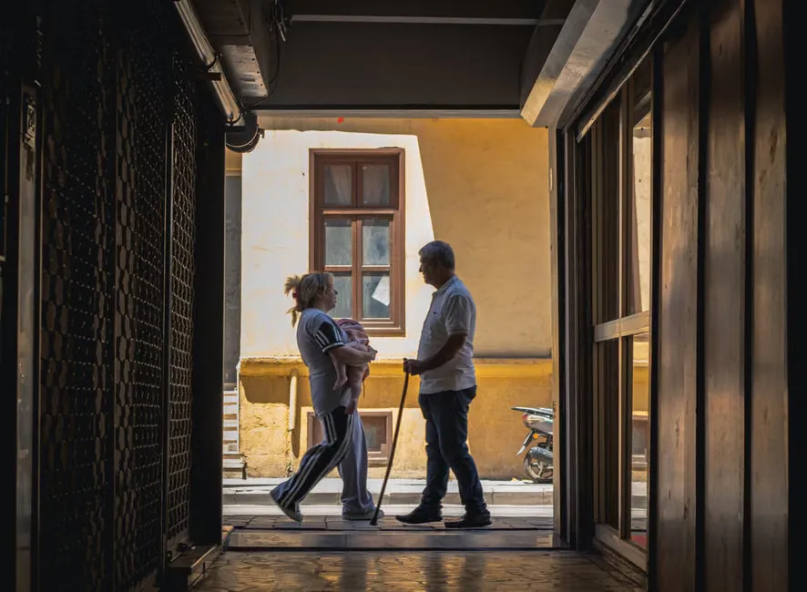 Caregiver walking beside a resident using a walking frame through a sunlit dining room