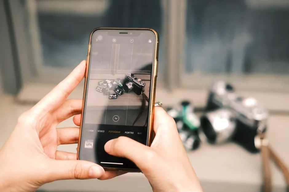 A close-up shot of hands using a smartphone to photograph vintage cameras.